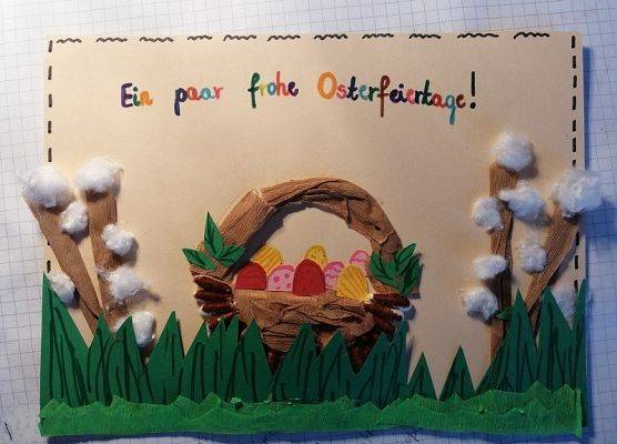 Kartka wielkanocna. Na górze kartki napis w języku niemieckim Wesołych Świąt Wielkanocnych. Na dole karki trawa na której jest koszyk z pisankami. Po obu stronach koszyka bazie