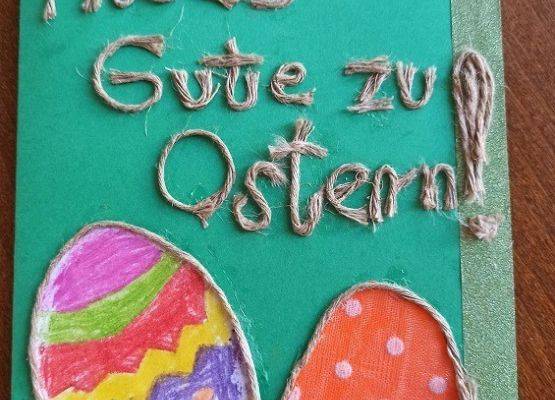 Kartka wielkanocna. Na zielonej kartce wyklejany ze sznurka napis w języku niemieckim. Wszystkiego najlepszego z okazji Świąt Wielkanocnych. Pod napisem dwie pisanki