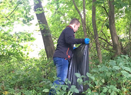 Uczeń trzyma worek na śmieci podczas akcji sprzątania świata. Wokół drzewa.
