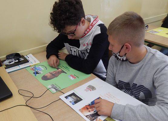 Dwóch uczniów klasy 7. Siedzą przy ławce szkolnej i wykonują projekt plastyczny z języka niemieckiego