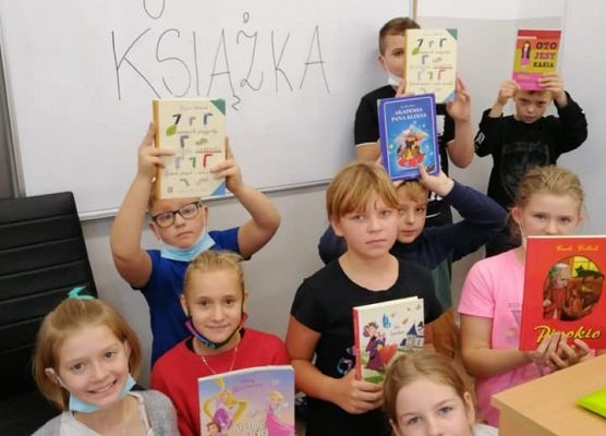 Na zdjęciu dzieci trzymające w rękach swoje ulubione książki. W tle biała tablica z napisem - Moja ulubiona książka