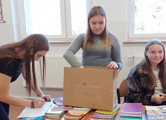 Na zdjęciu trzy dziewczęta pakują materiały plastyczne do kartonu.