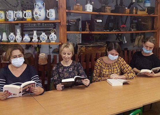 Na świetlicy szkolnej cztery kobiety siedzą przy stolikach i czytają książki. W tle kaszubska chatka