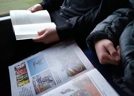 W autobusie szkolnym dwoje uczniów trzyma książki na kolanach i czyta