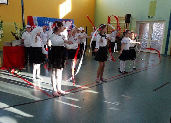 Uczennice klasy drugiej podczas tańca. Dziewczynki trzymają w dłoniach białe i czerwone wstążki.
