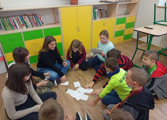 Uczniowie siędzą w kole. Na podłodze leżą wróżby andrzejkowe