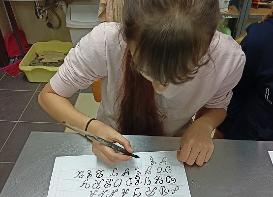 Uczennica starannie i estetycznie pisze literki na dużej kartce