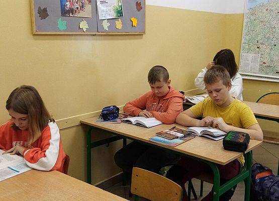 Czworo uczniów siedzi w ławkach szkolnych i czyta książki