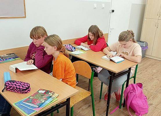 Czworo uczniów siedzi w ławkach szkolnych i czytają książki