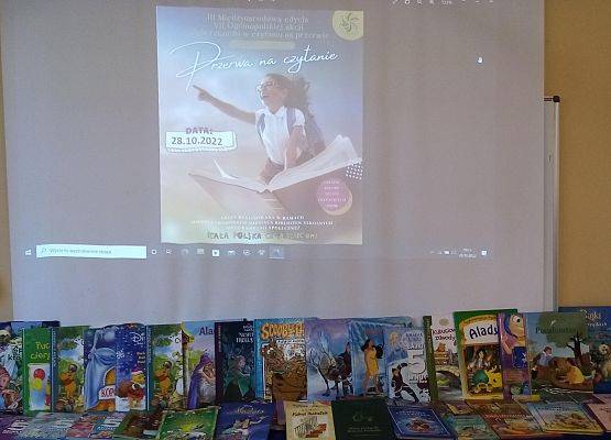 Wystawka książek dla dzieci z postaciami z bajek. W tle wyślietlony na ekranie plakat akcji Przerwa na czytanie.