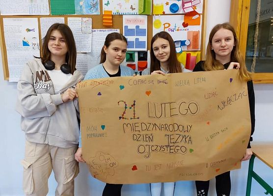 Cztery uczennice trzymają zrobiony przez nie plakat z okazji Miedzynarodowego Dnia Jezyka Ojczystego. Na plakacie znajduje się poprawna wymowa najczęściej popełnianych błędów językowych.